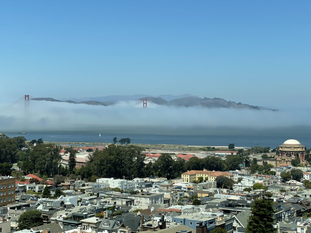 Fog rolling across the San Francisco Bay with the Golden Gate Bridge visible above the clouds and the Palace of Fine Arts in the foreground.