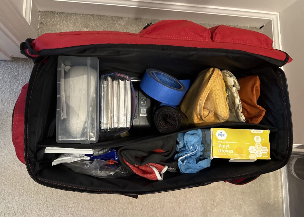 Open organizing bag containing painter’s tape, gloves, pouches, and supply cases.